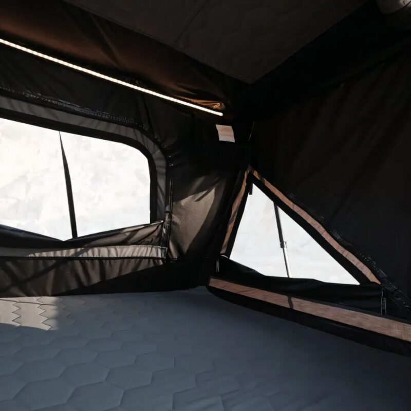 Image of the interior of the car rooftop tent, which can accommodate 2 to 3 people. It has a lot of space, and a large LED strip about two fingers wide, that expands across the ceiling parallel to the entrance.