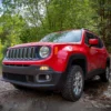 Right side view image of a red Jeep Renegade lifted 40mm, in the woods.