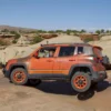 Side view image of an orange Jeep Renegade lifted 40mm, on the rocks.