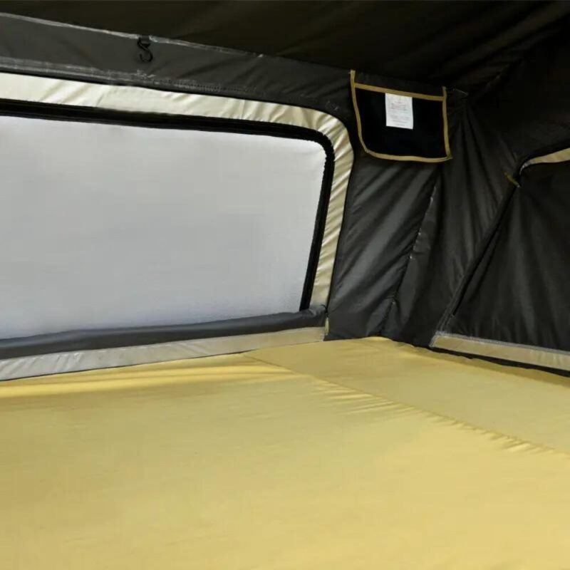 The interior of the 2-3 People Car Roof Top Tent Normandy Auto 140 by WildLand. It has a yellow mattress, a third even larger window facing the entrance, large windows left and right and storage pockets hanging from the walls.