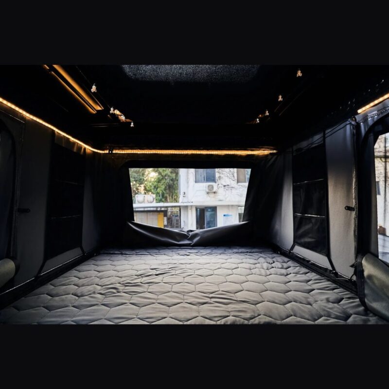 The interior of the second floor of the 4x4 Safari Cruiser roof top tent with the single-piece mesh window closed. Comfortable mattress covering the entire floor with a hatch leading to the lower floor and perimeter interior LED lights on the ceiling.