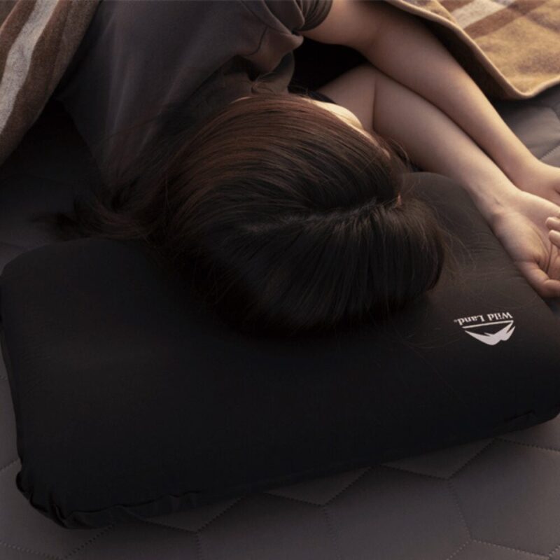 Close-up of a woman sleeping on the Self-Inflating Foam Pillow. It has a white wild land logo, black in color, about 2 heads wide.