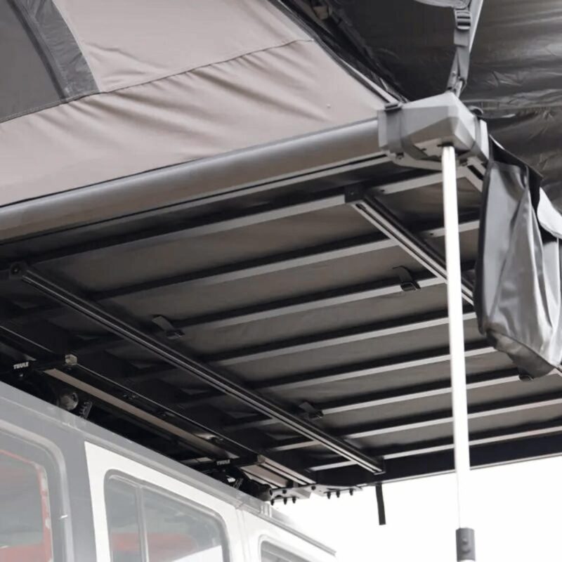 Close-up photo of the lower part of the eave of the Car Rooftop Tent 4-6 People Wild Cruiser 250 - WildLand. It protrudes from the car as much as the door opening and a little more, and is supported by 2 sturdy aluminum beams.