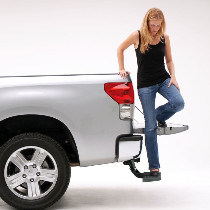 Image showing a woman stepping on the trunk bed with the help of the Toyota Hilux 2015+ Retractable Rear Bumper Steel Step